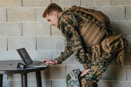 Foto de Soldado estadounidense en uniforme militar usando computadora portátil para el control de drones y para mantenerse en contacto con amigos y familiares. - Imagen libre de derechos