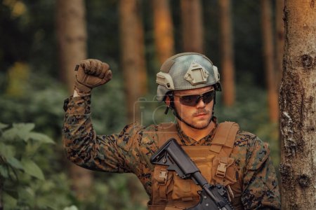 Téléchargez les photos : Soldat de guerre moderne officier montre des signaux tactiques de la main pour donner silencieusement des ordres et des alers pour équipe équipe forêt environnementoment. - en image libre de droit