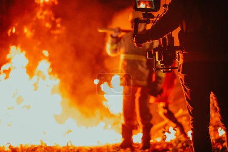 Foto de Un camarógrafo con equipo profesional y estabilización para la cámara que graba al bombero mientras realiza trabajos en un bosque en llamas. - Imagen libre de derechos