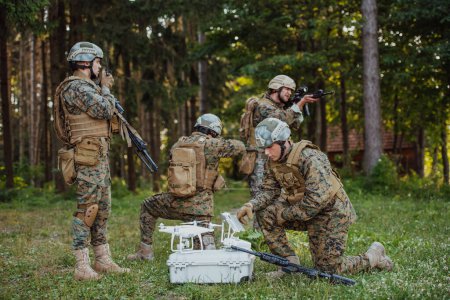 Foto de El escuadrón de soldados de guerra moderna está usando aviones no tripulados para explorar y vigilar durante la operación militar en el bosque. - Imagen libre de derechos