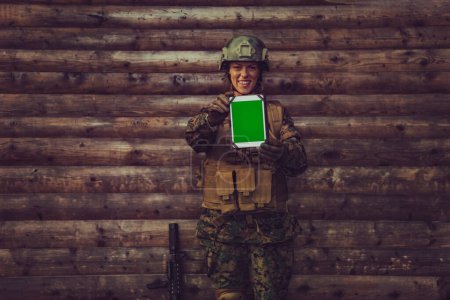 Téléchargez les photos : Femme soldat utilisant tablette informatique contre vieux mur en bois dans le camp. - en image libre de droit