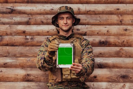 Photo for Soldier using tablet computer against old wooden wall in military camp to stay in contact with friends and family. - Royalty Free Image