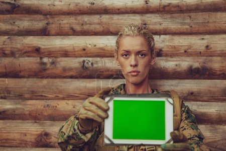 Photo for Woman soldier using tablet computer against old wooden wall in camp. - Royalty Free Image
