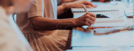 Photo for Closeup shot of business people hands using pen while taking notes on education training during business seminar at modern conference room. - Royalty Free Image