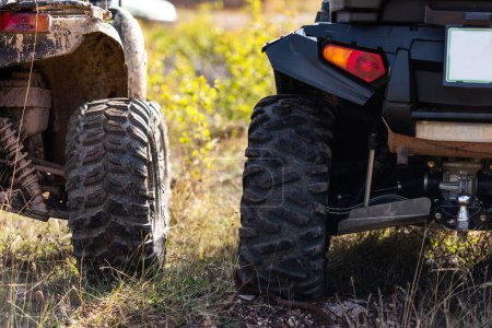 Close-up tail view of ATV quad bike on dirt country road. Dirty wheel of AWD all-terrain vehicle. Travel and adventure concept