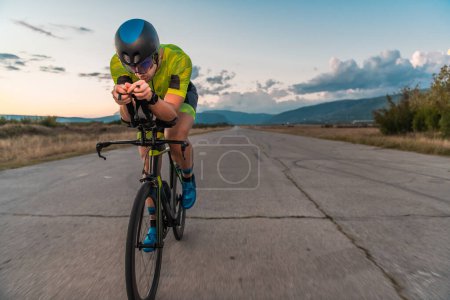 Foto de Triatleta montando su bicicleta al atardecer, preparándose para un maratón. Los colores cálidos del cielo proporcionan un hermoso telón de fondo para su esfuerzo decidido y centrado - Imagen libre de derechos