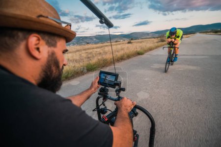 Photo for A videographer recording a triathlete riding his bike preparing for an upcoming marathon.Athletes physical endurance and the dedication required to succeed in the sport - Royalty Free Image