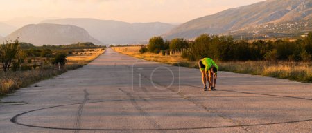 Photo for In the early morning light, the triathlete preparing for run by tying his shoes. With focused determination and unwavering dedication, he readies himself for the physical and mental challenge ahead - Royalty Free Image
