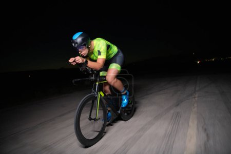 Photo for A triathlete rides his bike in the darkness of night, pushing himself to prepare for a marathon. The contrast between the darkness and the light of his bike creates a sense of drama and highlights the - Royalty Free Image