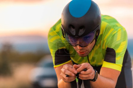 Photo for Close up photo of triathlete riding his bicycle during sunset, preparing for a marathon. The warm colors of the sky provide a beautiful backdrop for his determined and focused effort - Royalty Free Image