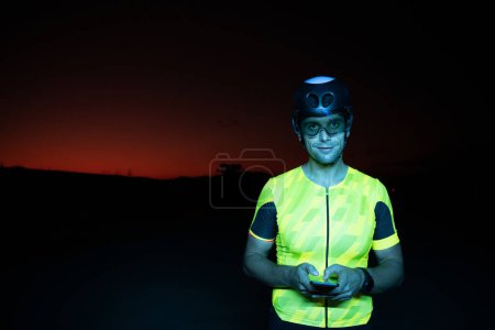 Photo for A triathlete using a smartphone while taking a break from a hard nights cycling training. High quality photo - Royalty Free Image