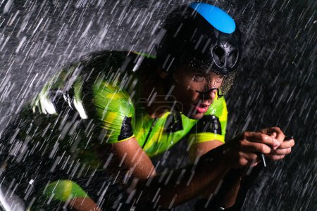 Photo for A triathlete braving the rain as he cycles through the night, preparing himself for the upcoming marathon. The blurred raindrops in the foreground and the dark, moody atmosphere in the background add - Royalty Free Image