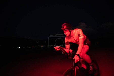 Photo for A triathlete rides his bike in the darkness of night, pushing himself to prepare for a marathon. The contrast between the darkness and the light of his bike creates a sense of drama and highlights the - Royalty Free Image