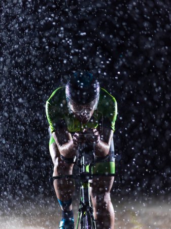 Foto de Un triatleta desafiando la lluvia mientras recorre la noche, preparándose para el próximo maratón. Las gotas de lluvia borrosas en primer plano y la atmósfera oscura y malhumorada en el fondo agregan - Imagen libre de derechos