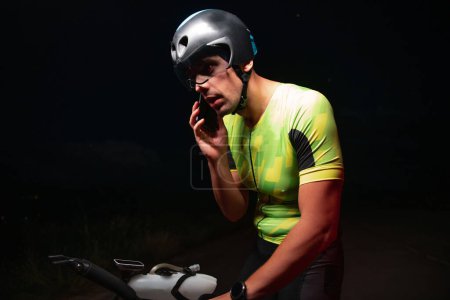 Téléchargez les photos : Un triathlète utilisant un smartphone tout en prenant une pause d'un entraînement de cyclisme de nuits difficiles. Photo de haute qualité - en image libre de droit