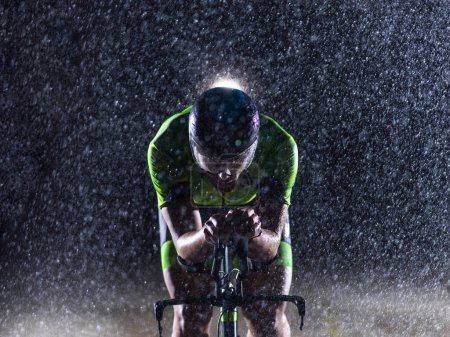 Foto de Un triatleta desafiando la lluvia mientras recorre la noche, preparándose para el próximo maratón. Las gotas de lluvia borrosas en primer plano y la atmósfera oscura y malhumorada en el fondo agregan - Imagen libre de derechos