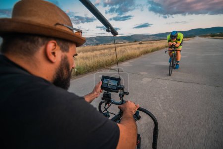 Téléchargez les photos : Un vidéaste enregistrant un triathlète en vélo se préparant pour un prochain marathon.Athlètes endurance physique et le dévouement nécessaire pour réussir dans le sport - en image libre de droit