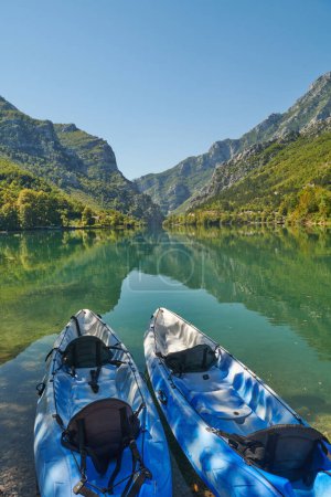 Photo for An idyllic photo of two kayaks on the river bank. In the background of green forest area and mountains. - Royalty Free Image