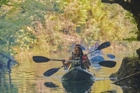 Photo for A group of friends enjoying having fun and kayaking while exploring the calm river, surrounding forest and large natural river canyons. - Royalty Free Image