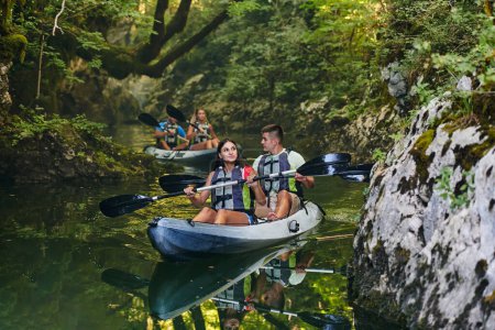 Photo for A group of friends enjoying having fun and kayaking while exploring the calm river, surrounding forest and large natural river canyons. - Royalty Free Image