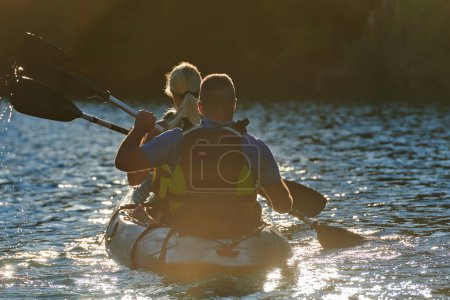 Téléchargez les photos : Un jeune couple profitant d'une balade idyllique en kayak au milieu d'une belle rivière entourée de verdure forestière au coucher du soleil. - en image libre de droit