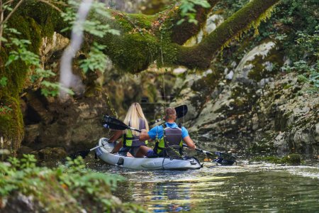 Foto de Una joven pareja disfrutando de un idílico paseo en kayak en medio de un hermoso río rodeado de vegetación forestal. - Imagen libre de derechos