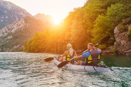 Téléchargez les photos : Un groupe d'amis profitant du plaisir et du kayak explorant la rivière calme, la forêt environnante et les grands canyons naturels de la rivière lors d'un coucher de soleil idyllique - en image libre de droit