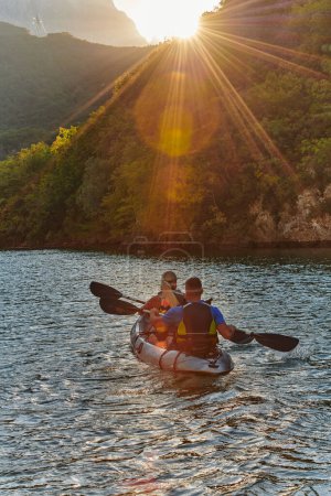Foto de Una joven pareja disfrutando de un idílico paseo en kayak en medio de un hermoso río rodeado de vegetación forestal al atardecer. - Imagen libre de derechos