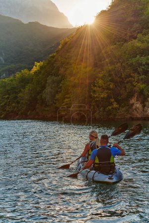 Foto de Una joven pareja disfrutando de un idílico paseo en kayak en medio de un hermoso río rodeado de vegetación forestal al atardecer. - Imagen libre de derechos