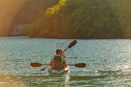 Téléchargez les photos : Un jeune couple profitant d'une balade idyllique en kayak au milieu d'une belle rivière entourée de verdure forestière au coucher du soleil. - en image libre de droit