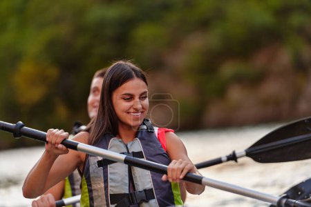 Téléchargez les photos : Un jeune couple profitant d'une balade en kayak idyllique au milieu d'une belle rivière entourée de verdure forestière. - en image libre de droit