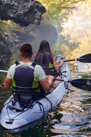 Photo for A young couple enjoying an idyllic kayak ride in the middle of a beautiful river surrounded by forest greenery. - Royalty Free Image