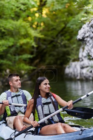 Foto de Una joven pareja disfrutando de un idílico paseo en kayak en medio de un hermoso río rodeado de vegetación forestal. - Imagen libre de derechos