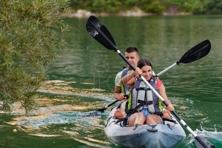 A young couple enjoying an idyllic kayak ride in the middle of a beautiful river surrounded by forest greenery. 
