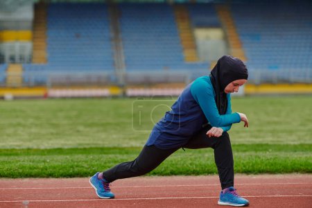 Téléchargez les photos : Une femme musulmane dans une burqa, une tenue de sport islamique, fait des exercices corporels, étirant son cou, ses jambes et son dos après une séance d'entraînement difficile sur le parcours du marathon - en image libre de droit