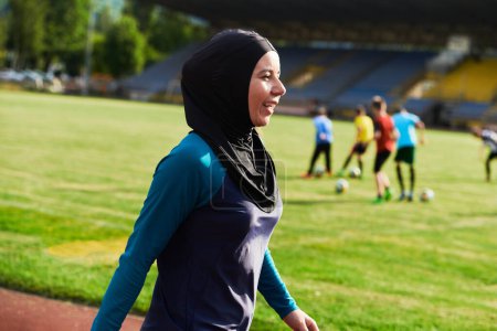Foto de Una mujer musulmana con una burka, una deportista islámica descansando después de una vigorosa sesión de entrenamiento en el curso de maratón. Una mujer hiyab se está preparando para una competencia maratónica. - Imagen libre de derechos