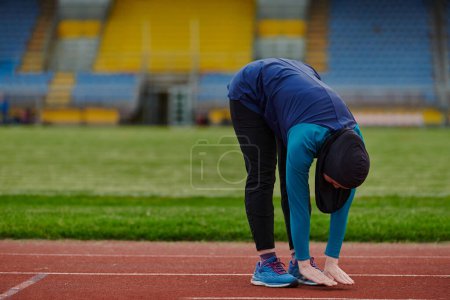 Photo for A Muslim woman in a burqa, an Islamic sports outfit, is doing body exercises, stretching her neck, legs and back after a hard training session on the marathon course - Royalty Free Image