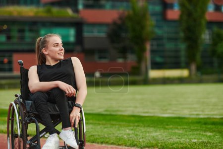 Photo for A smiling woman with disablitiy sitting in a wheelchair and resting on the marathon track after training. - Royalty Free Image