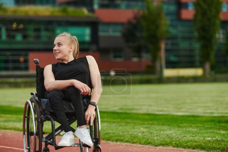 Téléchargez les photos : Une femme souriante avec une déficience assise dans un fauteuil roulant et se reposant sur la piste de marathon après l'entraînement. - en image libre de droit