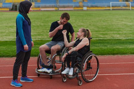Foto de Una mujer con una discapacidad en silla de ruedas hablando después de entrenar con una mujer que lleva un hijab y un hombre en silla de ruedas. - Imagen libre de derechos