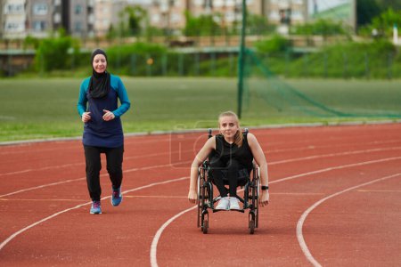 Foto de Una mujer musulmana en un burka corriendo junto con una mujer en silla de ruedas en el curso de maratón, preparándose para futuras competiciones - Imagen libre de derechos