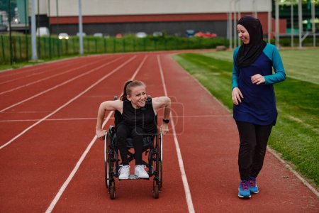 Foto de Una mujer musulmana en un burka corriendo junto con una mujer en silla de ruedas en el curso de maratón, preparándose para futuras competiciones - Imagen libre de derechos