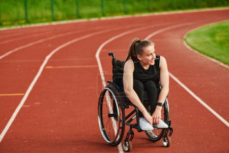 Foto de Una mujer sonriente con discapacidad sentada en una silla de ruedas y descansando en la pista de maratón después de entrenar. - Imagen libre de derechos