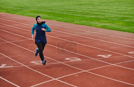 Foto de Una mujer musulmana en una burka viste ropa musulmana deportiva corriendo en un curso de maratón y preparándose para las próximas competiciones. - Imagen libre de derechos