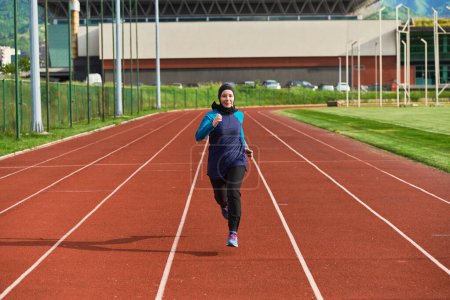 Foto de Una mujer musulmana en una burka viste ropa musulmana deportiva corriendo en un curso de maratón y preparándose para las próximas competiciones. - Imagen libre de derechos