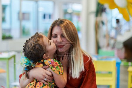 Téléchargez les photos : Une jolie petite fille embrasse et étreint sa mère à l'école maternelle. Photo de haute qualité - en image libre de droit