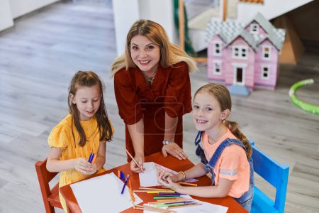 Photo for Creative kids during an art class in a daycare center or elementary school classroom drawing with female teacher - Royalty Free Image