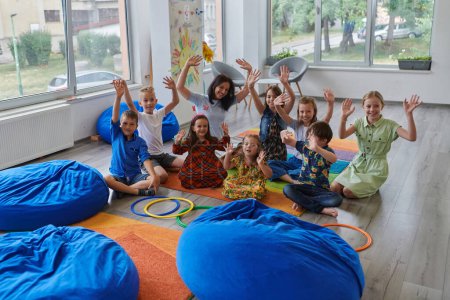 Foto de Una maestra feliz sentada y jugando juegos de manos con un grupo de niños pequeños. - Imagen libre de derechos