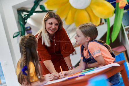 Photo for Creative kids during an art class in a daycare center or elementary school classroom drawing with female teacher - Royalty Free Image