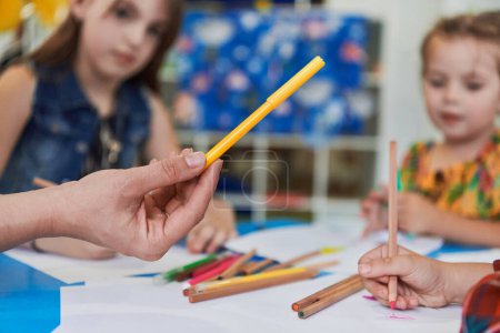 Photo for Close up photo of kids during an art class in a daycare center or elementary school classroom drawing with female teacher - Royalty Free Image